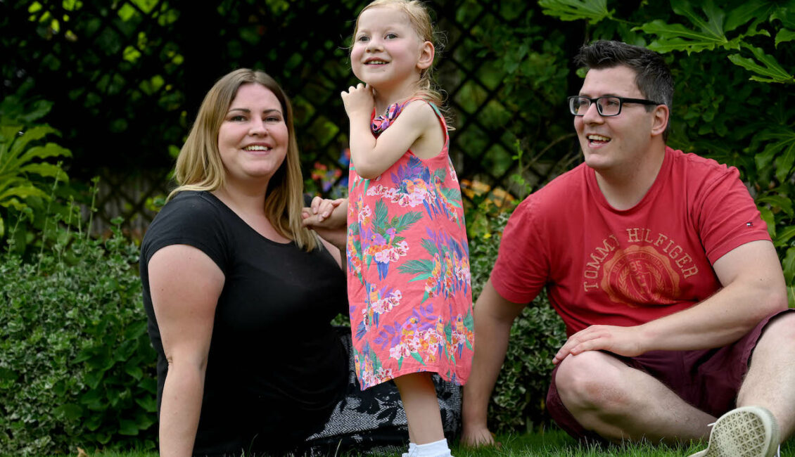 A family - a man and woman sitting either side of a little girl.